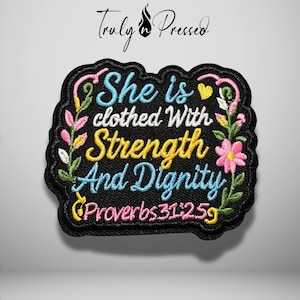 May include: A black embroidered patch featuring the text "She is clothed With Strength And Dignity Proverbs 31:25" in blue, white, and yellow thread. The design is framed by colorful floral vines with pink, yellow, and white flowers and green leaves.