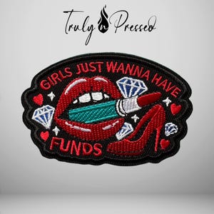 May include: An oval embroidered patch with a black background featuring red lips holding a teal lipstick, a red high-heeled shoe, and diamond icons. The text reads "GIRLS JUST WANNA HAVE FUNDS" in red embroidery. The brand name "Truly Pressed" appears above.