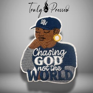 May include: An embroidered patch featuring a person with brown skin wearing a dark blue baseball cap with white lettering and a gold hoop earring. The patch displays the white embroidered text Chasing GOD not the WORLD on a dark blue background.