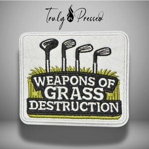 May include: Embroidered patch featuring golf clubs above the text "WEAPONS OF GRASS DESTRUCTION." The patch has a white background with a green and yellow border and grass design. The text is in black and white.