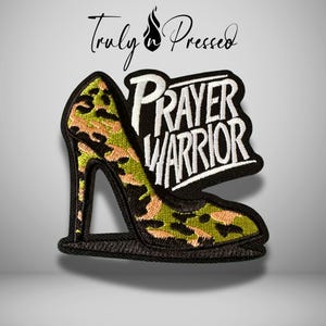May include: Embroidered patch featuring a high-heeled shoe with a camouflage pattern in green, black, and tan. The patch includes the words "PRAYER WARRIOR" in white lettering on a black background. The brand name "Truly Pressed" is above the shoe.