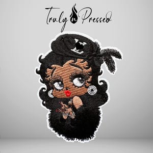 May include: An embroidered patch featuring a cartoon character with dark hair, large eyes, and red lips, wearing a black hat with a feather and a black heart emblem. The character has tan skin and is wearing white hoop earrings. The text Truly Pressed is above.