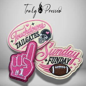 May include: Three embroidered patches featuring pink and black text and graphics. One oval patch reads Touchdowns Tailgates with a football helmet. A foam finger patch displays #1. A third patch reads Sunday Funday with a football graphic.