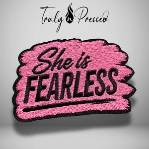 May include: An embroidered patch featuring a pink textured background with the black text 'She is FEARLESS' and a black border. Above the patch, the text 'Truly n Pressed' is displayed with a small flame icon between the two words.