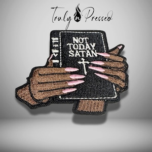 May include: Embroidered patch featuring a black book with the words "NOT TODAY SATAN" and a white cross. The book is held by hands with brown skin and long pink fingernails. The patch has a black border and the text "Truly Pressed" in cursive.