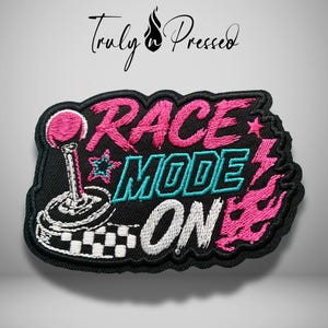 May include: A black embroidered patch featuring the text "RACE MODE ON" in pink, teal, and white thread. The design includes a gear shifter, a checkered flag pattern, a star, a lightning bolt, and flames. The brand name "Truly n Pressed" is visible.