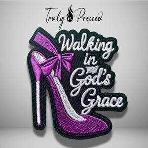 May include: An embroidered patch featuring a purple high-heeled shoe with a bow and the white stitched text Walking in God's Grace. The design is set against a black background with a black border, and the brand name Truly Pressed is at the top.