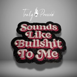 May include: Embroidered patch with the phrase "Sounds Like Bullshit To Me" in white and pink lettering. The patch has a black border with glitter accents and the words "Truly n Pressed" in script.