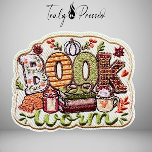 May include: An embroidered patch featuring the text "BOOK worm" in stylized lettering. The design includes a stack of books, a pair of glasses, a lit candle, a mug with a heart, and a pumpkin, all surrounded by autumn leaves and foliage.