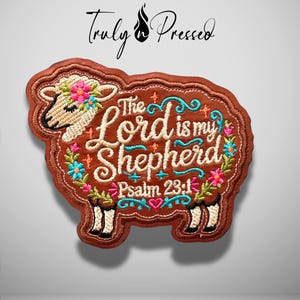 May include: A brown sheep-shaped embroidered patch featuring the text The Lord is my Shepherd Psalm 23:1 in white and teal thread. The design includes colorful floral accents in pink, blue, and green, with a cream-colored sheep head.