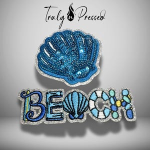 May include: A blue sequined seashell patch and a separate embroidered patch spelling the word BEACH, where the letter A is replaced by a seashell and the letter H is formed by blue and yellow circular shapes, all with silver glitter borders.
