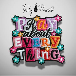 May include: A square embroidered patch featuring the text "PRAY about EVERYTHING" in a mix of block and script fonts. The letters are set against colorful rectangular backgrounds in shades of pink, purple, orange, and blue, accented with small teal, pink, and yellow flowers.