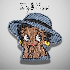 May include: An embroidered patch featuring a cartoon character with black hair, large eyes, and yellow hoop earrings, wearing a blue denim-textured hat with a black band. The text Truly n Pressed is printed in black above the patch.