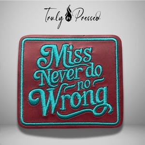 May include: A square patch with a deep maroon background and a teal embroidered border. The text "Miss Never do no Wrong" is stitched in a teal, cursive-style font across the center. The brand name "Truly Pressed" appears in black above.