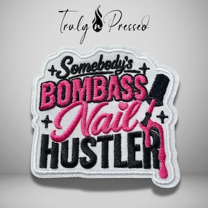 May include: An embroidered patch with a white background and black border. It features the text "Somebody's BOMBASS Nail HUSTLER" in black and pink thread. A black nail polish bottle with pink polish dripping down is on the right side.