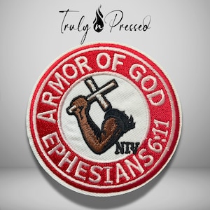 May include: A circular embroidered patch with a white center and a red border. The text reads ARMOR OF GOD EPHESIANS 6:11 and NIV. The center features an embroidered brown arm holding a white cross. The logo Truly Pressed is visible above.
