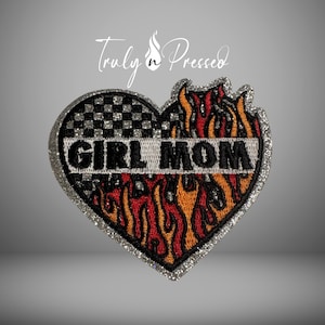 May include: Heart-shaped patch with the words "GIRL MOM" in black, outlined in silver glitter. The top left section features a black and white checkered pattern, while the bottom and right sides are designed with flames in red and orange.