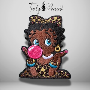 May include: An embroidered patch featuring a cartoon character with dark skin, black hair, and blue eyes blowing a bright pink bubble. The character wears a leopard print dress and hair bow, gold hoop earrings, and blue bracelets. Text reads Truly n Pressed.