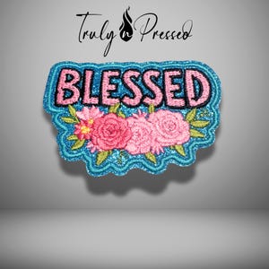 May include: An embroidered patch featuring the word BLESSED in pink letters with a black outline, set against a shimmering blue background. Below the text are three pink roses with green leaves and stems, all bordered by a wavy blue edge.