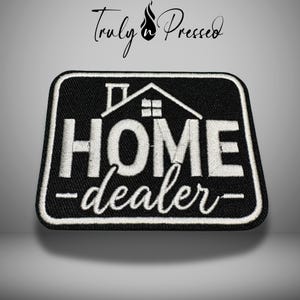 May include: Black and white embroidered patch with the words "HOME dealer" and a house graphic. The patch has a rectangular shape with rounded corners and a white border. The text is in a bold, stylized font.