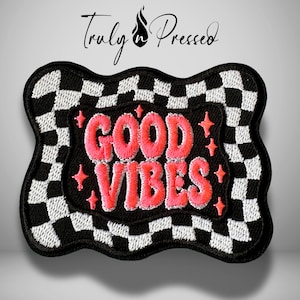 May include: An embroidered patch with a wavy, black and white checkered border. The center is black with the text "GOOD VIBES" stitched in bright pink thread, surrounded by small pink star-shaped accents. The brand name "Truly n Pressed" is above.