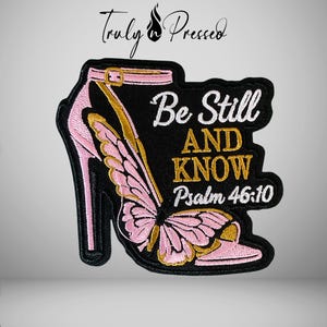 May include: An embroidered patch featuring a high-heeled shoe with pink butterfly wings, gold accents, and the white and gold text Be Still AND KNOW Psalm 46:10. The design is set against a black background with a black stitched border.
