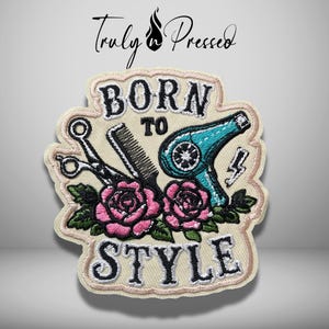 May include: An embroidered patch with a cream background featuring the text BORN TO STYLE in black. The design includes a pair of black scissors, a black comb, a teal hair dryer, a small lightning bolt, and two pink roses with green leaves.