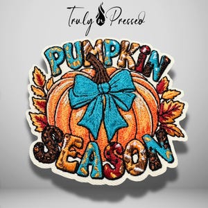May include: An embroidered patch featuring an orange pumpkin with a bright blue bow, surrounded by autumn leaves. The text PUMPKIN SEASON is stitched in a multi-colored, textured font above and below the pumpkin. The design has a white border.