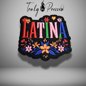 May include: Embroidered patch with the word "LATINA" in colorful letters. The patch is black with a floral design in red, orange, pink, and blue. The text "Truly Pressed" is at the top.