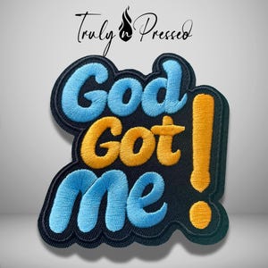 May include: An embroidered patch featuring the text God Got Me! in a bold, layered style. The words God and me are stitched in light blue thread, while the word Got and the exclamation point are in golden yellow, all on a black background.
