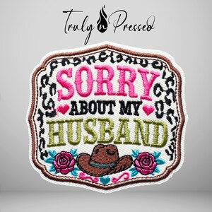 May include: A rectangular embroidered patch with a brown border featuring a black leopard print pattern. The text reads SORRY ABOUT MY HUSBAND in pink and green. Below the text is a brown cowboy hat flanked by two pink roses with teal leaves.