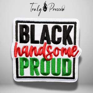 May include: A square embroidered patch with a white background and a black border. The text reads BLACK in black block letters, handsome in red cursive script, and PROUD in green block letters. The design is centered within a black rectangular frame.