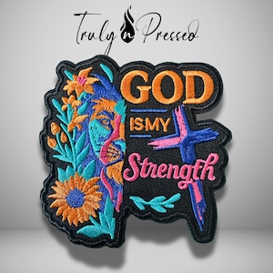 May include: Embroidered patch with a lion design, sunflowers, and the text "GOD IS MY STRENGTH." The patch features orange, blue, and pink colors on a black background. The brand name "Truly Pressed" is at the top.