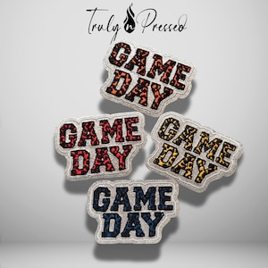 May include: Four embroidered patches with the text "GAME DAY" in a block font. Each patch features a different color leopard print pattern: orange, red, yellow, and blue. The patches have a silver glitter border and the logo "Truly Pressed" above.