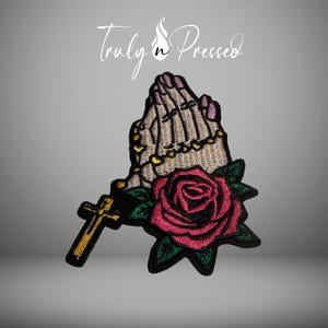 May include: Embroidered patch featuring praying hands with a rosary and a red rose. The hands have a skeletal appearance, with gold-colored beads on the rosary and a gold cross. The patch is outlined in black, with the text "Truly n Pressed".
