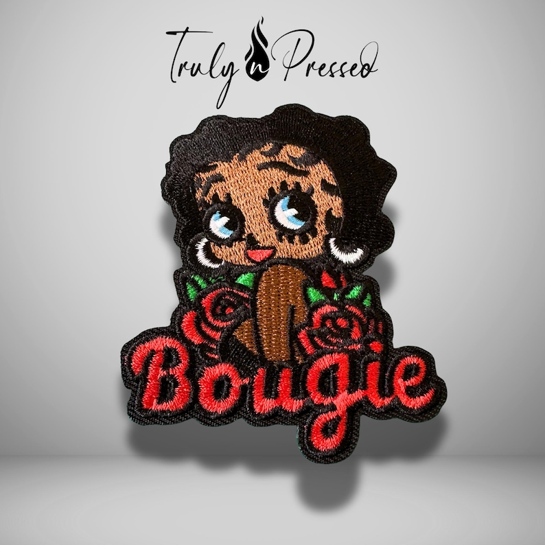 May include: An embroidered patch featuring a cartoon character with black hair, large blue eyes, and hoop earrings, surrounded by red roses and green leaves. The word Bougie is stitched in red cursive script below the character. The text Truly Pressed is above.