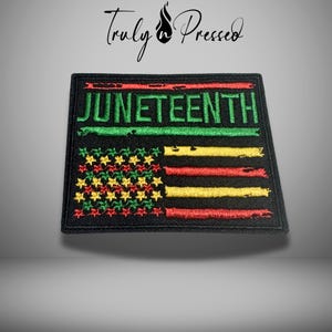 May include: A rectangular black embroidered patch featuring the word JUNETEENTH in green capital letters. Below the text is a stylized flag design with a field of green, yellow, and red stars on the left and horizontal stripes in those colors.