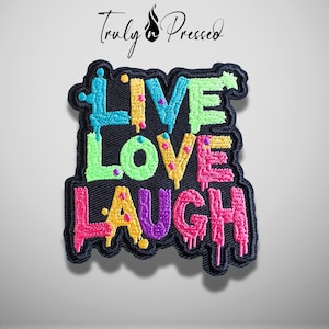 May include: A black embroidered patch featuring the text LIVE LOVE LAUGH in a dripping, multi-colored font. The letters are stitched in bright shades of blue, yellow, green, pink, and purple against a dark background with a black border.