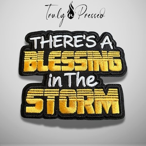 May include: An embroidered patch with a black background and a black border. The text reads THERE'S A in white, BLESSING in yellow, in The in white, and STORM in yellow. The Truly n Pressed logo is visible at the top of the image.