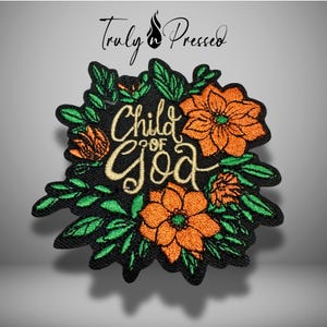 May include: An embroidered patch featuring the text "Child of God" in gold cursive lettering, surrounded by orange flowers and green leaves on a black background. The brand name "Truly Pressed" is printed in black text above the patch design.