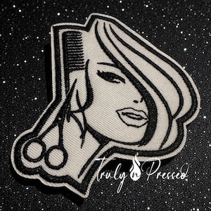 May include: A black and white patch featuring a stylized illustration of a woman's face with long hair, a comb, and scissors. The text "Truly n' Pressed" is written in cursive below the image.