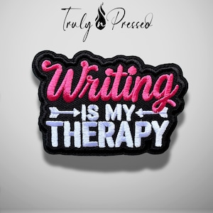 May include: A black embroidered patch with a scalloped edge featuring the pink cursive text Writing and the white block text IS MY THERAPY. A white arrow graphic separates the two lines of text. The brand name Truly n Pressed is above.