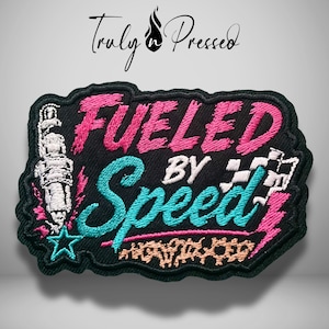 May include: A black embroidered patch featuring the text FUELED BY SPEED in pink and teal thread. The design includes a white spark plug, a checkered flag, a teal star, and a pink lightning bolt on a black background with a black border.