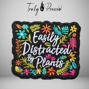 May include: A black embroidered patch with a scalloped edge featuring the white text "Easily Distracted By Plants" surrounded by colorful embroidered botanical elements including various flowers and leaves in shades of orange, pink, yellow, and blue.