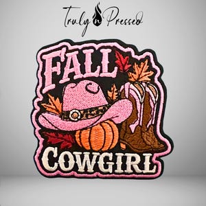 May include: An embroidered patch featuring the text FALL COWGIRL in pink and white. The design includes a pink cowboy hat with a leopard print band, a bright orange pumpkin, brown cowboy boots, and colorful autumn leaves on a black background.