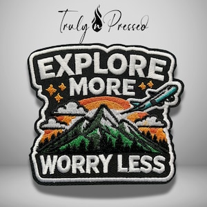 May include: An embroidered patch featuring the text EXPLORE MORE WORRY LESS in white block letters. The design includes a green mountain range, orange sunset, white clouds, and a teal airplane flying against a black background with gold stars.