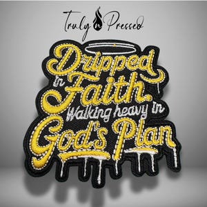 May include: Black embroidered patch with the text "Dripped in Faith Walking heavy in God's Plan" in yellow script. The patch has a black border and white dripping accents. The brand name "Truly Pressed" is at the top.