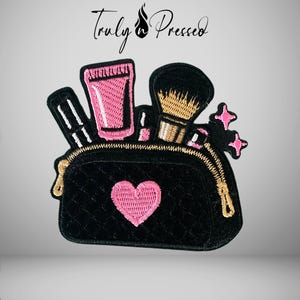 May include: An embroidered patch featuring a black quilted makeup bag with a pink heart, containing a pink tube, a makeup brush, and other cosmetic items. The design includes two small pink star accents and the text Truly n Pressed above it.