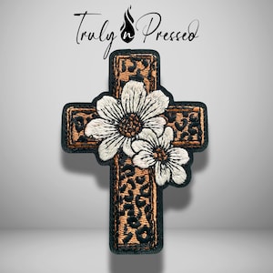 May include: An embroidered cross patch featuring a brown and black leopard print pattern. Two white daisies with yellow centers are stitched over the center of the cross. The text Truly n Pressed is printed in black above the cross design.