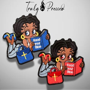 May include: Two embroidered patches featuring a cartoon character with black hair, gold hoop earrings, and light blue pants, lying down while reading a book. One patch has a blue book and bag with a yellow cross, the other a red book and bag.